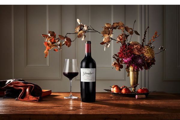 A bottle of Heritage Clone cabernet sauvignon sits on a table with a vase of dried flowers. 