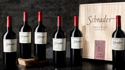 A man opening a branded Schrader box with bottles of Schrader wines on the wall behind him.