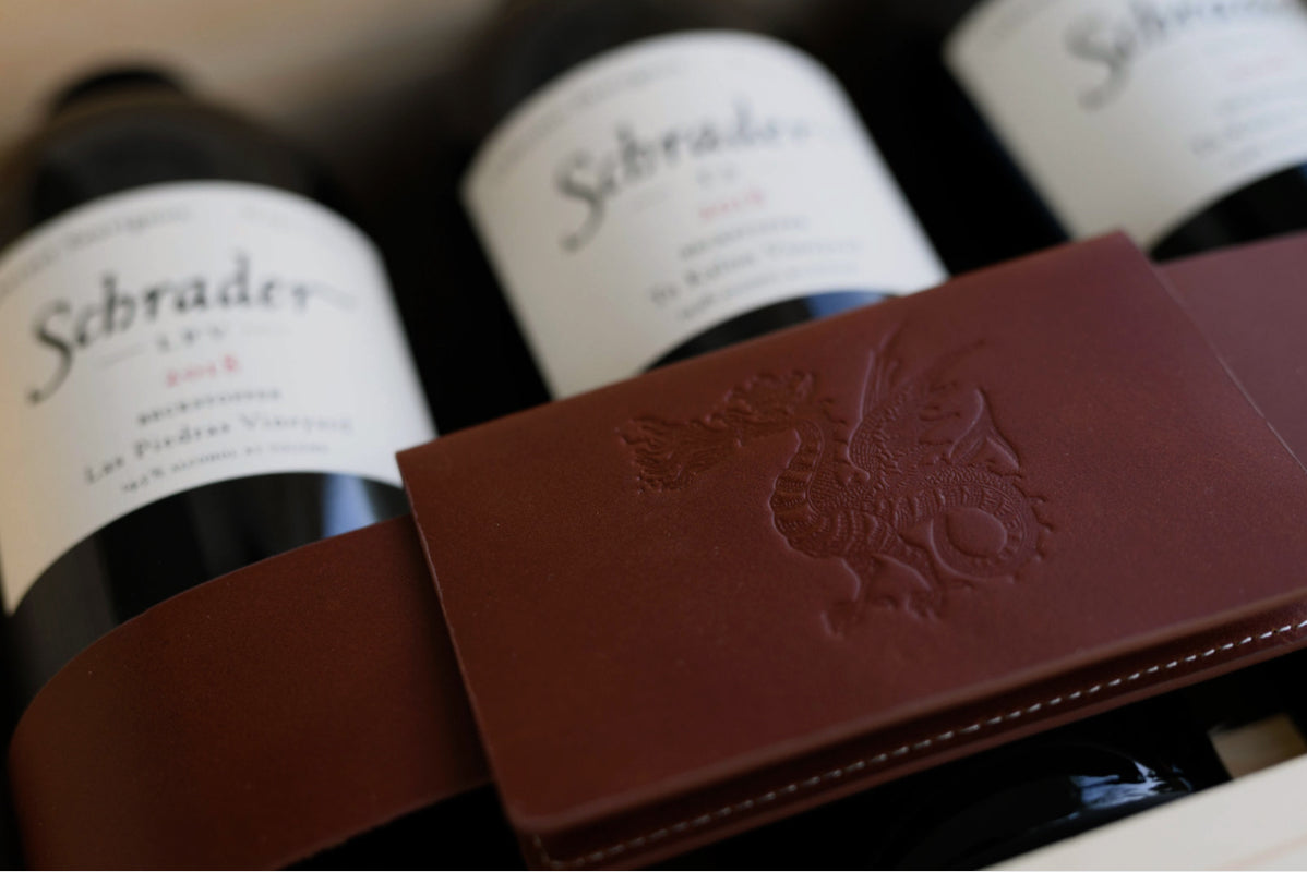 Image of bottles of Schrader wine laying down under a leather belt with the Schrader logo on it